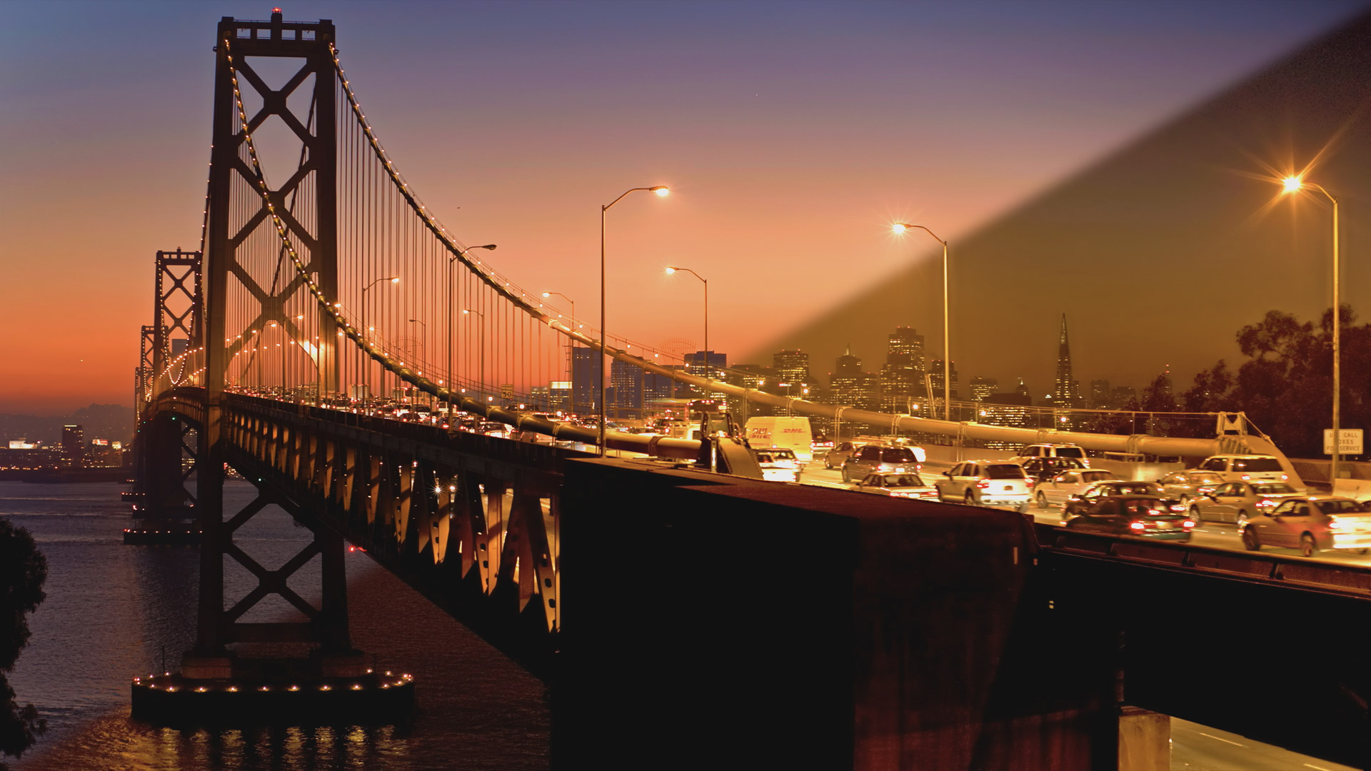 San Francisco Bay Bridge traffic at dusk with skyline behind traffic and bay